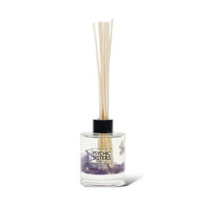 May include: A clear glass diffuser bottle with a black cap and wooden reeds. The bottle contains purple flower petals and the text "PSYCHIC SISTERS LONDON".
