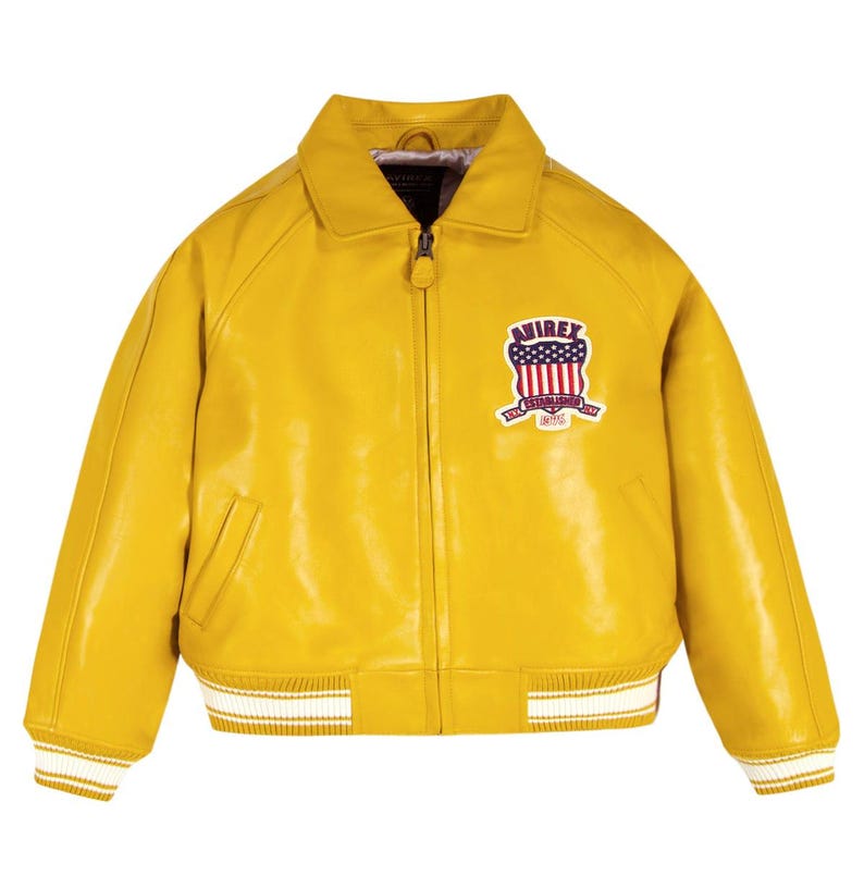 May include: A bright yellow leather jacket with a collared neckline and a zipper closure. The jacket features a white and red patch on the chest with the text "AVIREX ESTABLISHED 1975". The cuffs and hem have white stripes.