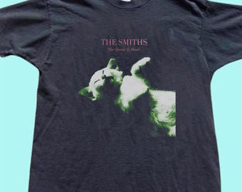 May include: Dark gray t-shirt featuring the band name "THE SMITHS" and the album title "The Queen Is Dead" in pink text. The shirt displays a green and white image of a cat.