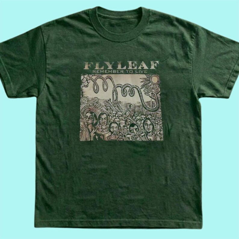Puede incluir: Una camiseta de manga corta de color verde oscuro con un estampado gr&aacute;fico en el pecho. El estampado muestra el texto "FLYLEAF" y "REMEMBER TO LIVE" sobre una ilustraci&oacute;n de una serpiente enroscada y una multitud de personas.