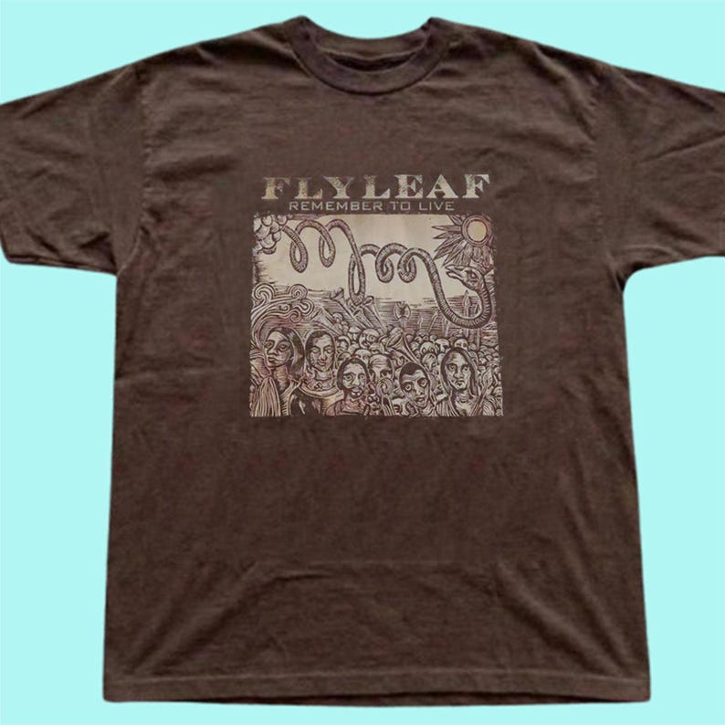 Puede incluir: Una camiseta de manga corta de color marr&oacute;n oscuro con un estampado gr&aacute;fico en el pecho. El estampado muestra el texto FLYLEAF REMEMBER TO LIVE sobre una ilustraci&oacute;n de una multitud de personas, una serpiente enroscada y un sol.