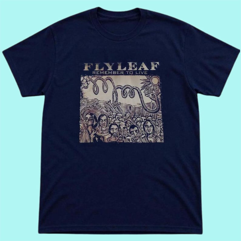 Puede incluir: Una camiseta azul marino de manga corta con un estampado gr&aacute;fico en el pecho. El estampado muestra el texto "FLY LEAF" y "REMEMBER TO LIVE" sobre una ilustraci&oacute;n de una serpiente enroscada, un sol y una multitud de personas.