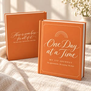 May include: Two orange hardcover books with white text. The front book reads "One Day at a Time MY IVF JOURNEY The appointments. The waiting. The hope." The back book reads "There is room here for all of it. The brave days. The hard days. Your days."