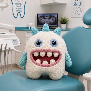 May include: A plush crochet monster toy with a fuzzy white body, light blue horns and arms, and a wide pink mouth featuring four upper and three lower white teeth. The creature has large round eyes with black pupils and light blue crocheted borders.