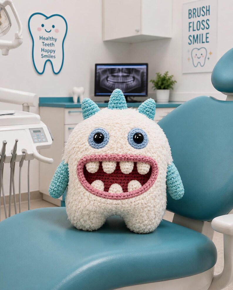 May include: A plush crochet monster toy with a fuzzy white body, light blue horns and arms, and a wide pink mouth featuring four upper and three lower white teeth. The creature has large round eyes with black pupils and light blue crocheted borders.