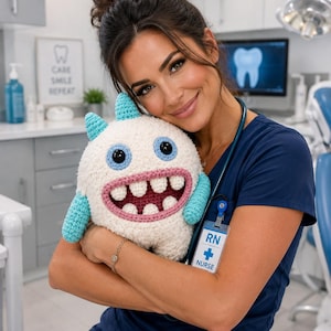 May include: A round, white crocheted monster plush toy with two light blue horns, light blue arms, and large black eyes. The monster features a wide, open mouth with a pink border and four large white teeth, showcasing a friendly, soft-textured design.