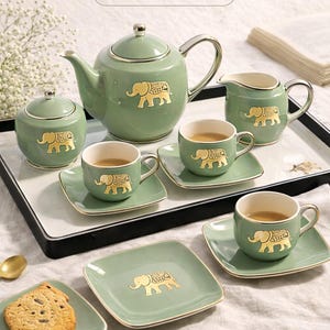 May include: A luxury tea set mockup featuring a green teapot, sugar bowl, creamer, cups, and saucers. Each piece has a gold elephant design. The set is arranged on a tray with a cookie and the text "LUXURY TEA SET MOCKUPS" and "DIGITAL DOWNLOAD".