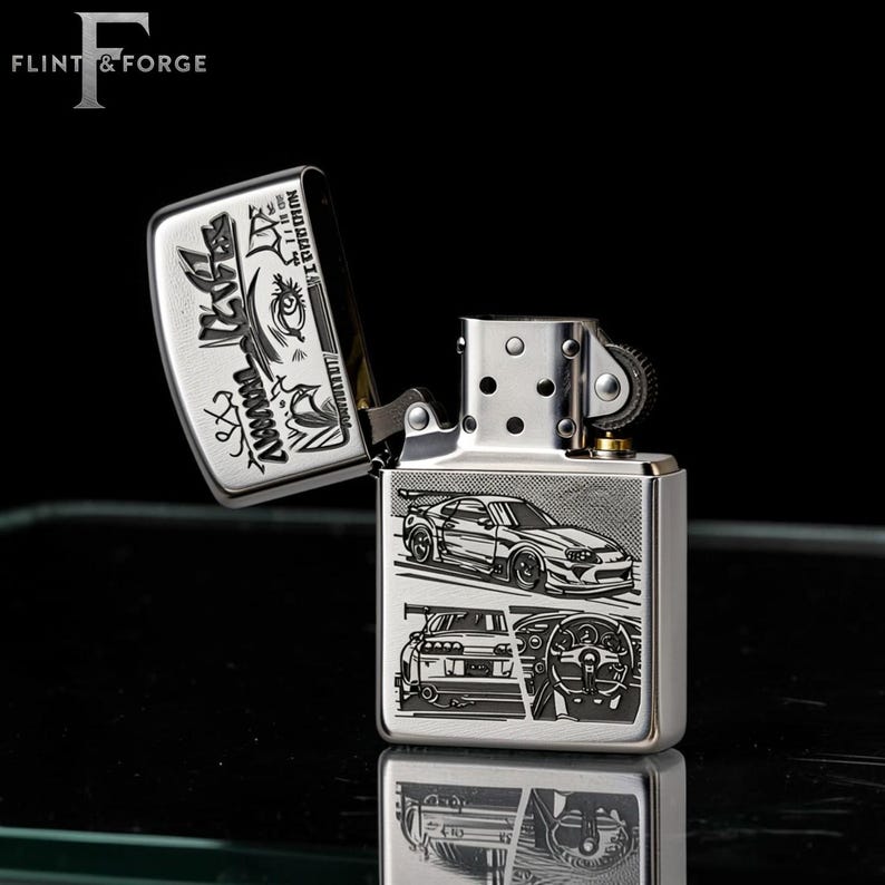 May include: A silver-colored lighter with an open lid, featuring engraved car designs. The lighter's body displays a car, its rear, and a steering wheel. The lid has Japanese text and graphic designs. The brand name "Flint & Forge" is at the top.