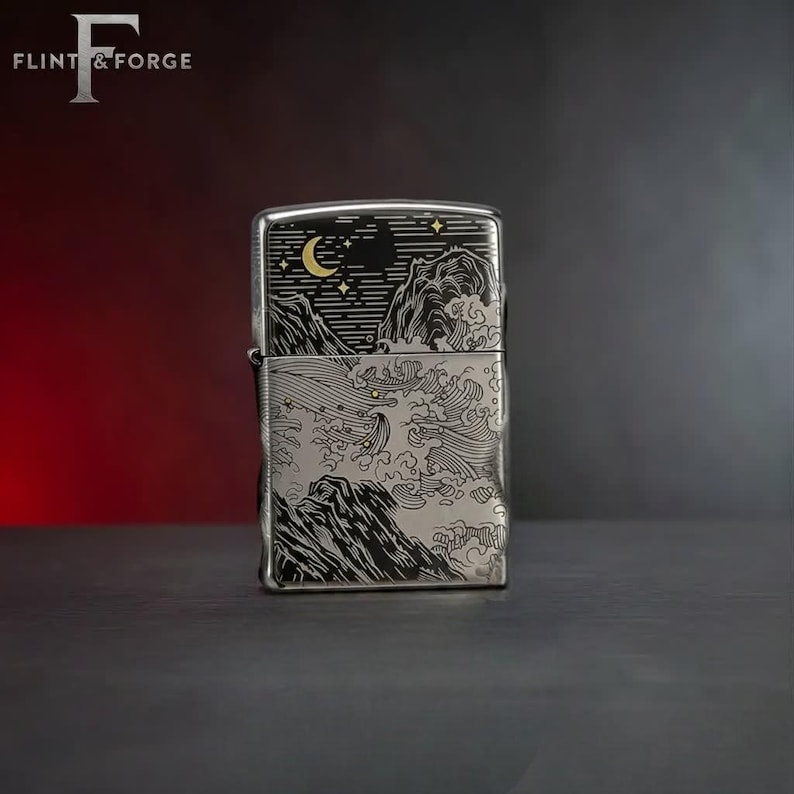 May include: A silver-colored lighter with a detailed engraved design. The design features a night scene with a crescent moon, stars, and stylized waves and mountains. The brand name "Flint & Forge" is at the top left.