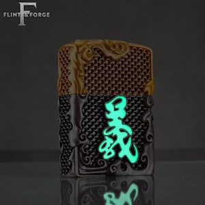 May include: A decorative lighter with a gold and brown top and a black bottom. The lighter features a glowing green design on the front. The Flint & Forge logo is in the top left corner.