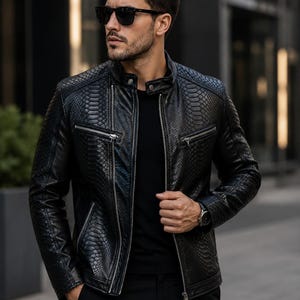 Puede incluir: Chaqueta de cuero negra con un patrón de piel de serpiente, con cuello alzado, bolsillos con cremallera y cierre de cremallera frontal. La chaqueta se lleva con una camisa y pantalones negros, y la persona lleva gafas de sol y un reloj.