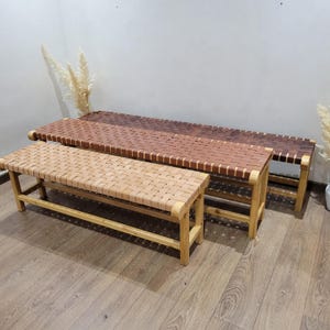 May include: Three wooden benches with woven leather seats in varying shades of brown. The benches have light-colored wooden legs and frames. The largest bench is in the background, with a medium-sized bench in the middle and a smaller bench in the foreground.