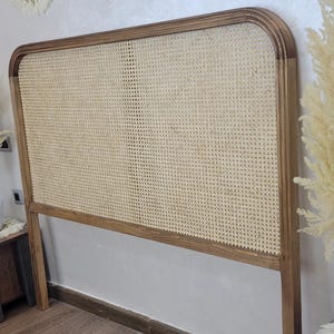 May include: A wooden headboard with a woven cane centre. The headboard has a rectangular shape with rounded corners and is made of light brown wood. Three circular wall hangings with fringed edges are above the headboard.