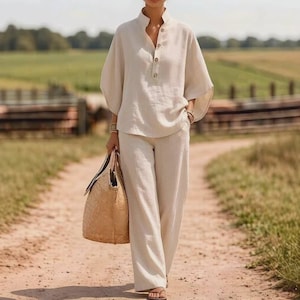 May include: A beige linen outfit consisting of a button-down shirt with short sleeves and wide-leg pants. The outfit is paired with a woven tote bag. The ensemble is suitable for warm weather and casual occasions.