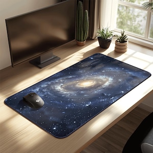 May include: A rectangular mouse mat displaying a detailed galaxy design with swirling blues, whites, and a golden core. A black computer mouse is positioned on the mat, which is placed on a wooden desk. The mat offers a smooth surface for mouse operation.