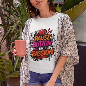 May include: White t-shirt with the text "No Pause Button on Passion" in red, pink, and black. The person is wearing a floral patterned kimono and holding a pink mug. The person is also wearing blue jean shorts.
