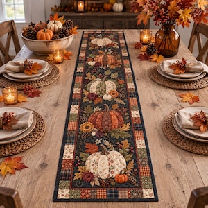 Könnte beinhalten: Ein rechteckiger Tischläufer mit dunklem Hintergrund und einem wiederkehrenden Muster aus Kürbissen, Herbstblättern, Sonnenblumen und Tannenzapfen. Der Läufer ist mit einem Patchwork-Design aus kleinen Quadraten in herbstlichen Farben umrandet.