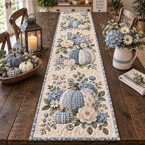 Può includere: Un runner da tavola trapuntato rettangolare con sfondo color crema e un motivo ripetuto di zucche in tessuto blu e bianco, grappoli di ortensie blu e margherite bianche, rifinito con un bordo in tessuto a motivi blu e bianchi.