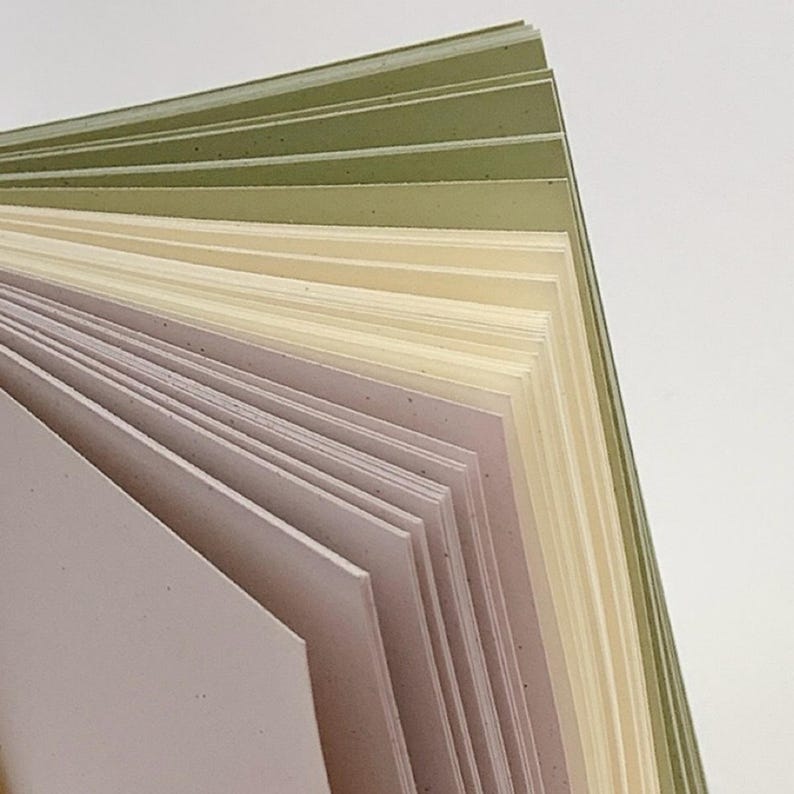 May include: A stack of rectangular paper sheets fanned out to display a gradient of colors. The sheets transition from a soft dusty pink at the front to a creamy off-white in the middle, ending with shades of sage green at the back edge.