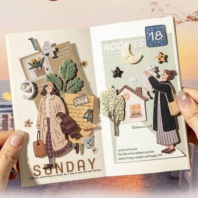 May include: An open journal page featuring layered paper collages, fabric stickers, and die-cut illustrations. The left side displays a person in a beige coat, the number 14, and the word SUNDAY. The right side shows a person holding a cat, a house, and the number 18.