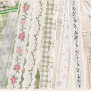May include: Five strips of decorative adhesive tape featuring various patterns: pink roses on a scalloped edge, white lily of the valley, a green and white gingham check, a white lace border with stars, and a thin strip with small green floral motifs.