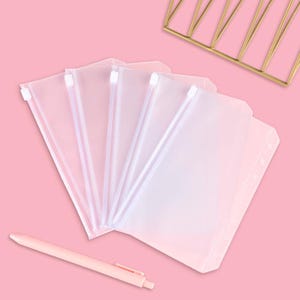 May include: A set of five translucent, frosted plastic zip pouches designed for a binder, featuring white plastic zip pulls and pre-punched holes along the side for insertion, accompanied by a single light pink retractable ballpoint pen.