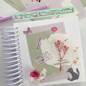 May include: A white spiral-bound notebook page decorated with layered paper scraps, a dried pink flower sprig, a butterfly sticker, a cat illustration, and text snippets including "I hope we can all be as brave as each other". A light purple pen lies nearby.