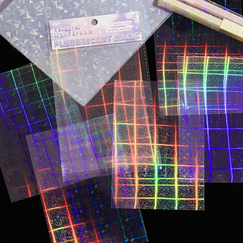 May include: A collection of transparent sheets featuring a holographic grid pattern that reflects rainbow colors. One sheet includes a header card with the text Colorful Light Dream and FLUORESCENT MAGIC. The sheets have a shimmering, iridescent finish.