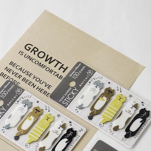 May include: Two packs of cat-shaped sticky notes on a tan card with the text GROWTH IS UNCOMFORTABLE BECAUSE YOU'VE NEVER BEEN HERE. Each pack contains 100 sheets with five different cat designs in white, brown, yellow, and black colors.