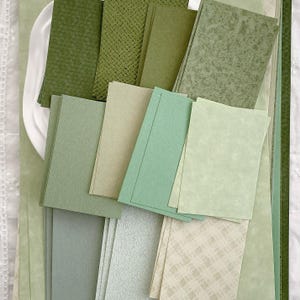 May include: A collection of rectangular paper sheets in various shades of green, including olive, sage, and mint. The papers feature diverse textures such as woven patterns, mottled finishes, smooth surfaces, and subtle grid designs in light green.