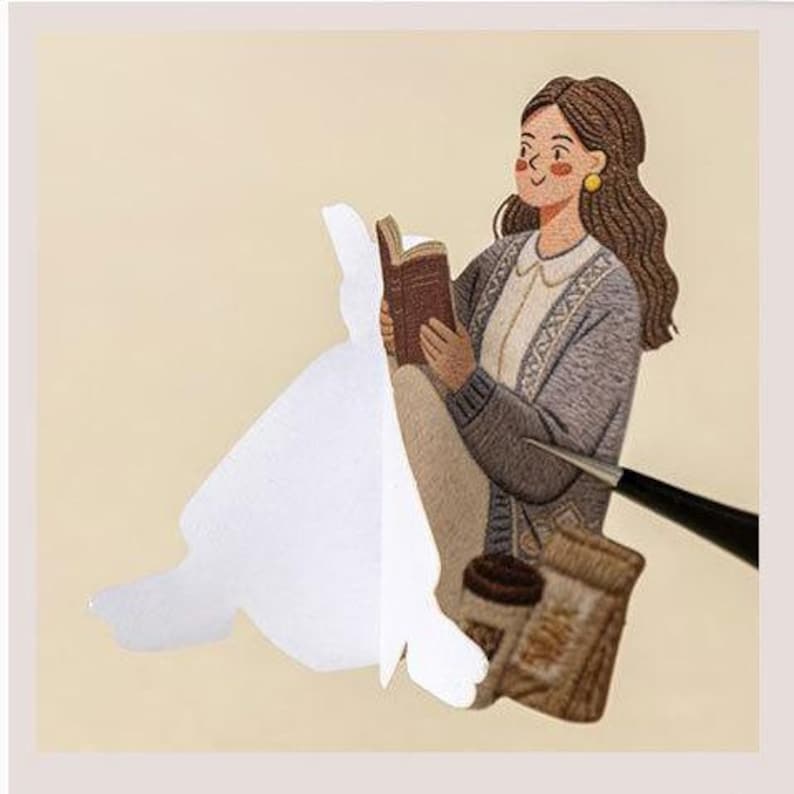 May include: An embroidered patch featuring a person with long brown hair wearing a grey cardigan over a white collared shirt, reading a brown book. Beside the person are a brown coffee cup and a small brown bag, partially covered by a white paper backing.