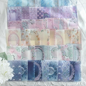 May include: A collection of rectangular translucent stickers featuring various designs including floral patterns, bows, frames, stars, moons, and clovers in shades of blue, purple, pink, and cream. The stickers are arranged in a grid-like layout.