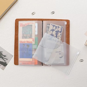 Puede incluir: Una funda de cuaderno de cuero marrón con fundas de plástico transparente para tarjetas. Las fundas contienen varias tarjetas rectangulares con gráficos y texto impresos, incluyendo las palabras "Save a skater's life" y "Silent Disco".