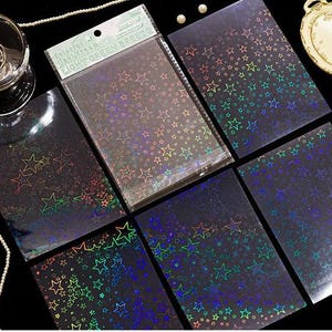 May include: A collection of rectangular sheets featuring a holographic star pattern on a dark background. The top sheet is enclosed in a clear plastic sleeve with a header card labeled "Colorful Light Film" and "LIGHT GREEN BREEZE" in green text.