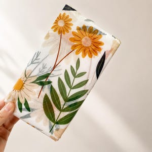 May include: A rectangular sheet of white tissue paper featuring a repeating botanical pattern of yellow and cream-colored daisy-like flowers with thin brown stems and dark green fern-like leaves printed across the surface of the paper.