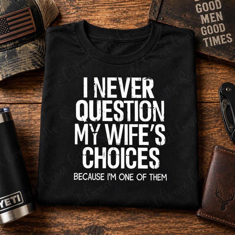May include: A black t-shirt featuring white distressed-style text that reads: I NEVER QUESTION MY WIFE'S CHOICES BECAUSE I'M ONE OF THEM. The shirt has a crew neckline and short sleeves, with the graphic centered on the front of the garment.