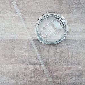 May include: A clear plastic drinking straw with a white lid on top of a stainless steel tumbler.