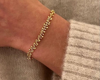 May include: A gold-toned bracelet featuring a delicate chain design adorned with numerous small, spherical beads arranged in a repeating pattern along the entire length of the jewelry piece, creating a textured and consistent metallic appearance.