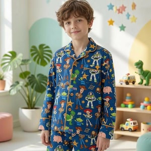 Könnte beinhalten: Blauer Schlafanzug mit Figuren aus dem Animationsfilm Toy Story. Das Set besteht aus einem Hemd mit Knöpfen und einer passenden Hose, beide mit Bildern von Woody, Buzz Lightyear und anderen Charakteren. Der Schlafanzug hat einen orangefarbenen Besatz.