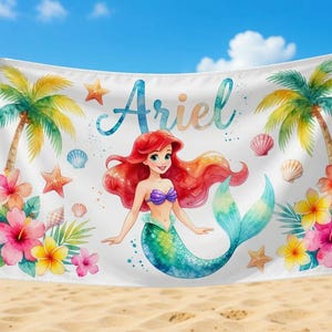 May include: White beach towel featuring a watercolor illustration of a mermaid with red hair, a purple top, and a teal tail. The towel is decorated with tropical flowers, palm trees, starfish, and the name "Ariel".