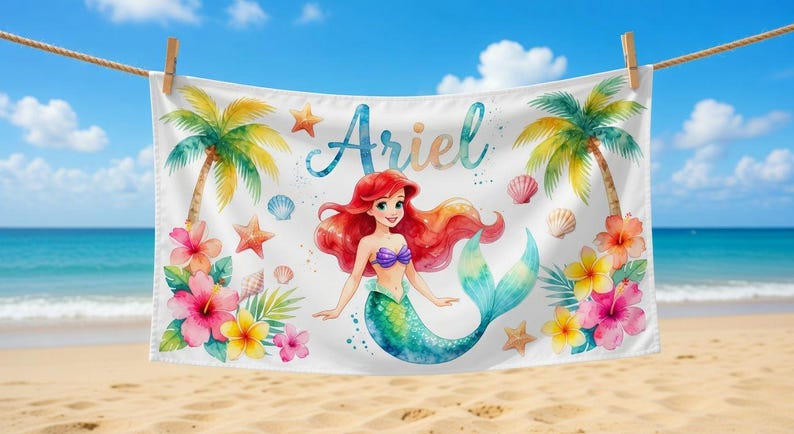 May include: White beach towel featuring a watercolor illustration of a mermaid with red hair, a purple top, and a teal tail. The towel is decorated with tropical flowers, palm trees, starfish, and the name "Ariel".