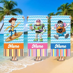 May include: Three beach towels featuring Toy Story characters. Each towel has a blue wave pattern background, a character image, and the word "Name" at the bottom. The towels are held up on a beach with palm trees.
