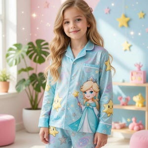 Könnte beinhalten: Hellblaues Pyjama-Set mit einem Prinzessinnen- und Sternen-Design. Das langärmlige Oberteil und die Hose zeigen eine Prinzessinnen-Illustration, Sterngrafiken und den Namen "Rosalina". Der Pyjama hat weiße Verzierungen und ist aus einem weichen Material gefertigt.