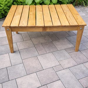May include: A rectangular wooden coffee table featuring a slatted top surface made of light brown planks. The table is supported by four straight legs, each attached to the frame with visible silver metal hardware at the top corners.