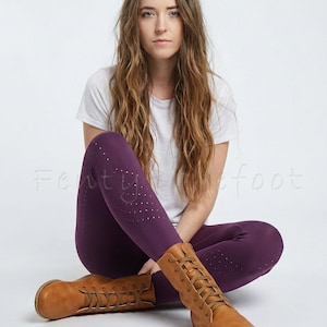 Op de afbeelding: Pruimkleurige legging met een stippenpatroon en bruine leren laarzen met veters. De legging wordt gecombineerd met een wit t-shirt. De laarzen hebben een ronde neus en een platte zool.
