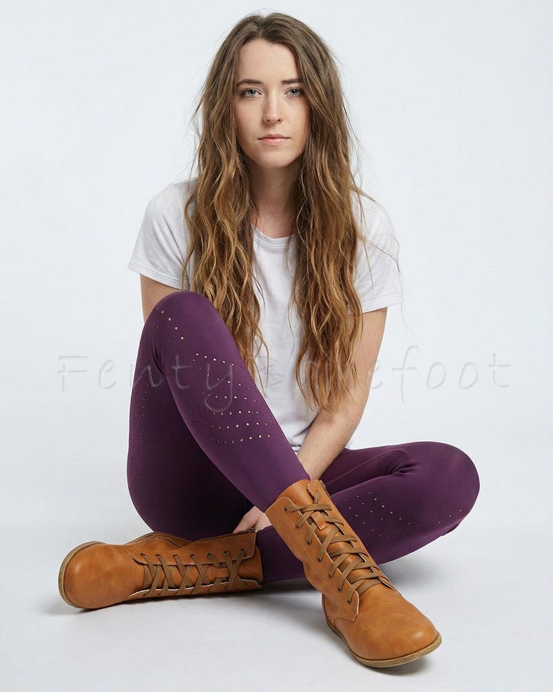 Op de afbeelding: Pruimkleurige legging met een stippenpatroon en bruine leren laarzen met veters. De legging wordt gecombineerd met een wit t-shirt. De laarzen hebben een ronde neus en een platte zool.
