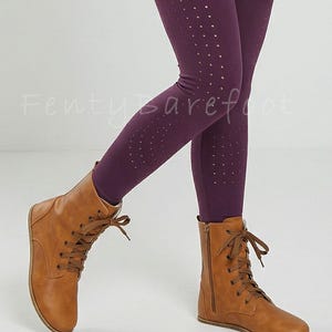 Op de afbeelding: Bruine leren veterlaarzen met een zijrits, gecombineerd met donkerpaarse leggings met een stippenpatroon. De leggings zijn zichtbaar vanaf de knie&euml;n. De tekst "Fenty Barefoot" is zichtbaar.