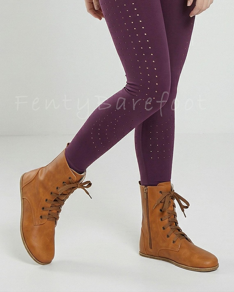 Op de afbeelding: Bruine leren veterlaarzen met een zijrits, gecombineerd met donkerpaarse leggings met een stippenpatroon. De leggings zijn zichtbaar vanaf de knie&euml;n. De tekst "Fenty Barefoot" is zichtbaar.