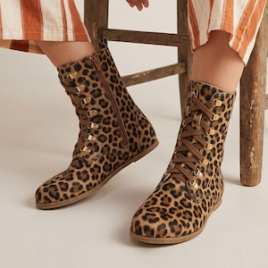 May include: A pair of leopard print boots with brown laces and gold-colored eyelets. The boots have a side zipper and are made of a soft, textured material. The boots are mid-calf height and have a flat sole.