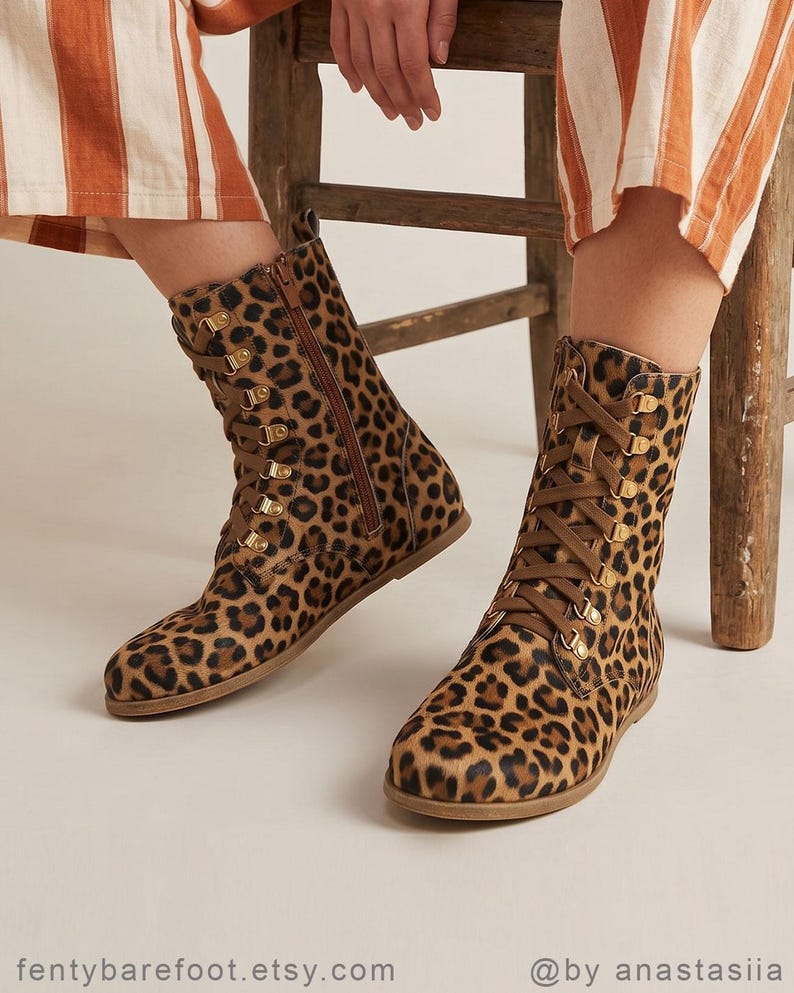 May include: A pair of leopard print boots with brown laces and gold-colored eyelets. The boots have a side zipper and are made of a soft, textured material. The boots are mid-calf height and have a flat sole.